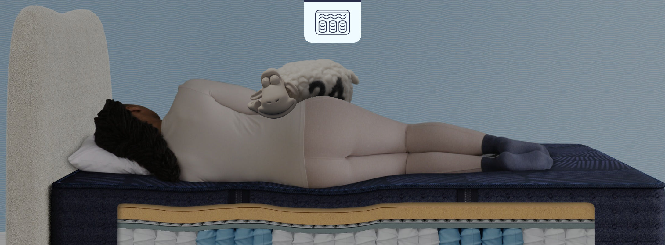 Person sleeping on a Serta hybrid mattress with a cutaway view showcasing its coil support and foam comfort layers, while a relaxed Serta sheep rests on top.