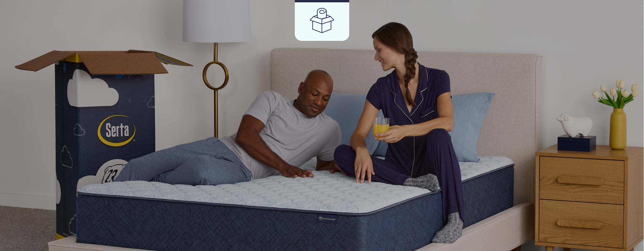 Serta Sleep to go mattress in box sitting in a beige bedframe with the packaging sitting on the floor to the left