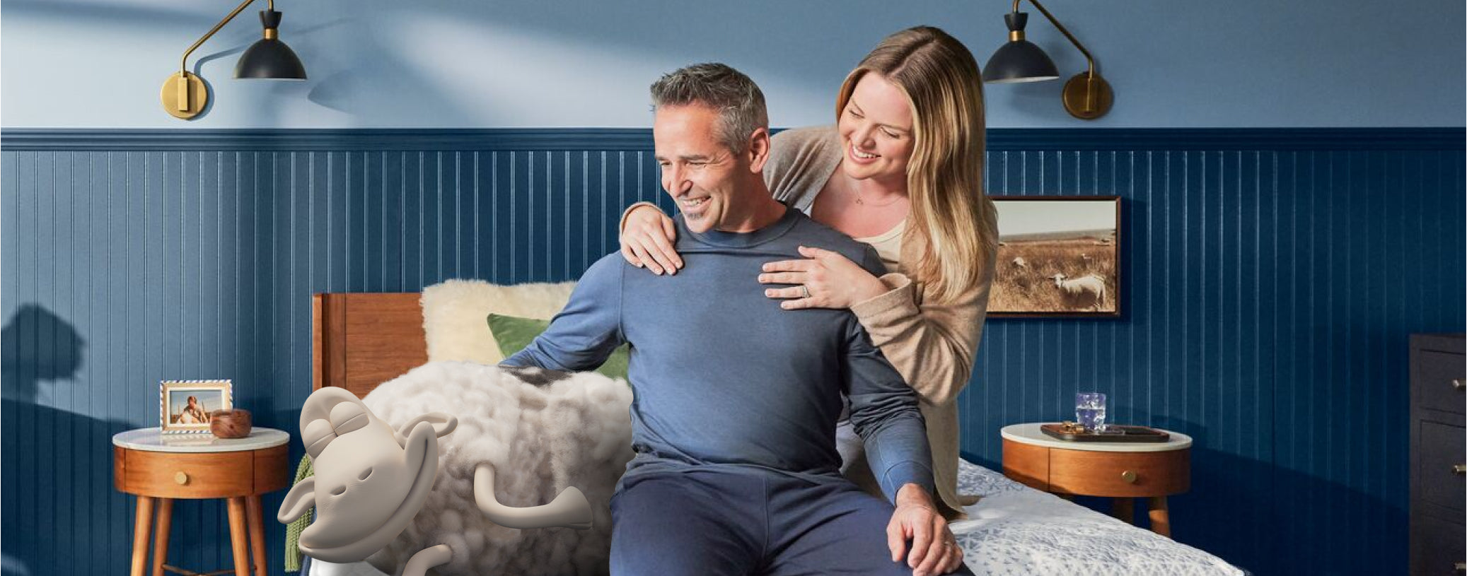 "A happy couple enjoys the comfort of a spacious California King mattress, designed for taller individuals or those who share their bed with pets, while a Serta sheep lounges playfully, adding a fun touch to the scene.