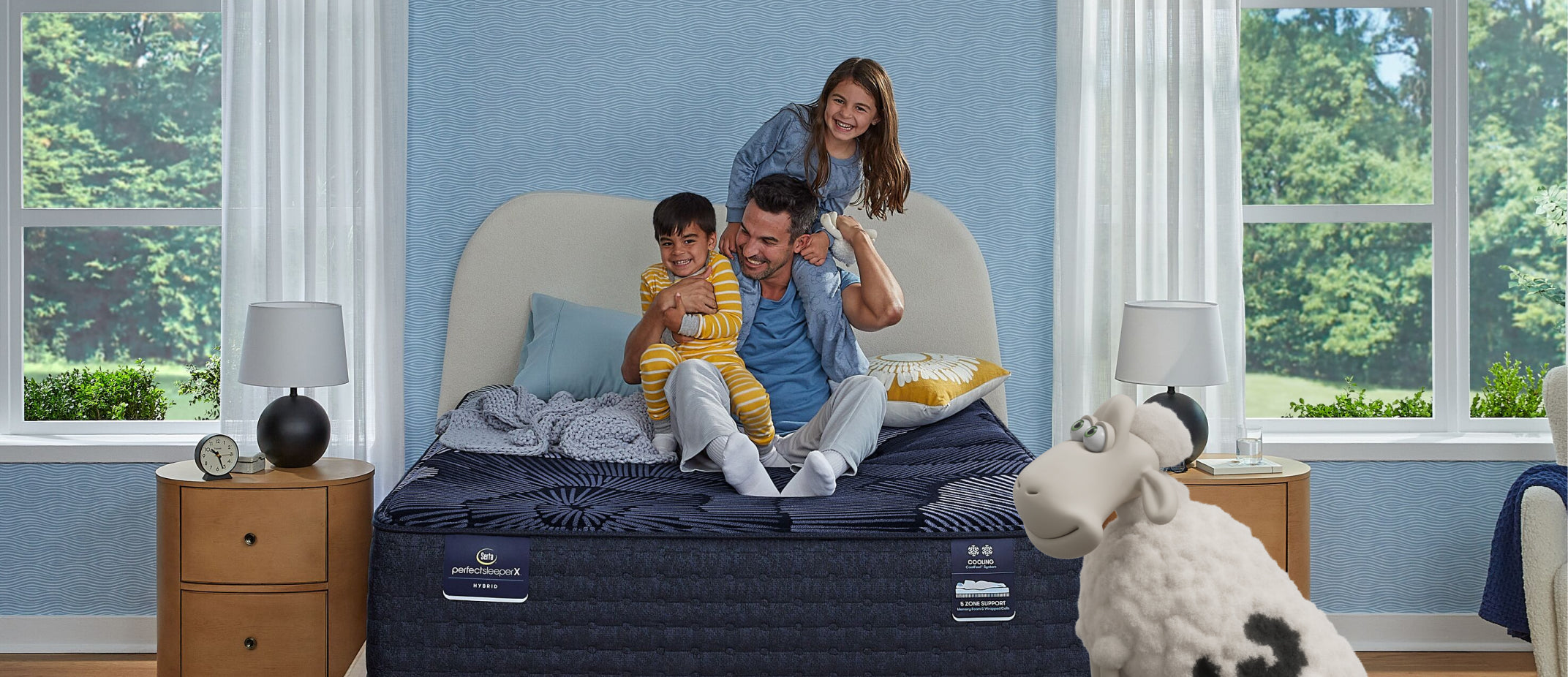 Smiling family sits on a full-size mattress, with a Serta sheep nearby.