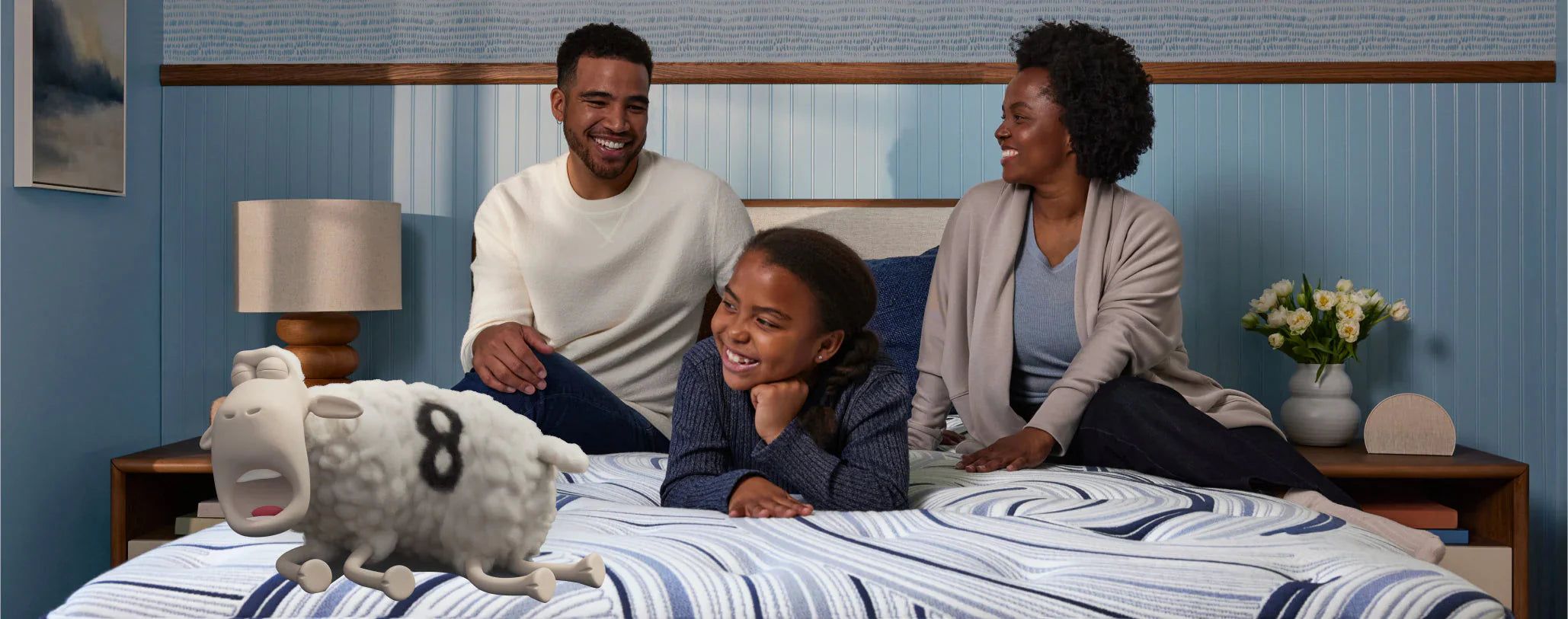 A smiling couple and their child enjoy quality time on a spacious Serta King mattress, with a playful Serta sheep adding a touch of fun