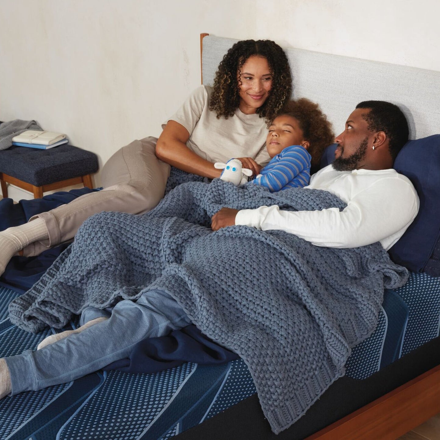 A family laying on a Serta iSeries medium blue mattress, woman on the left, boy in the middle holding a stuffed animal and a man on the right||feel: medium||level: standard