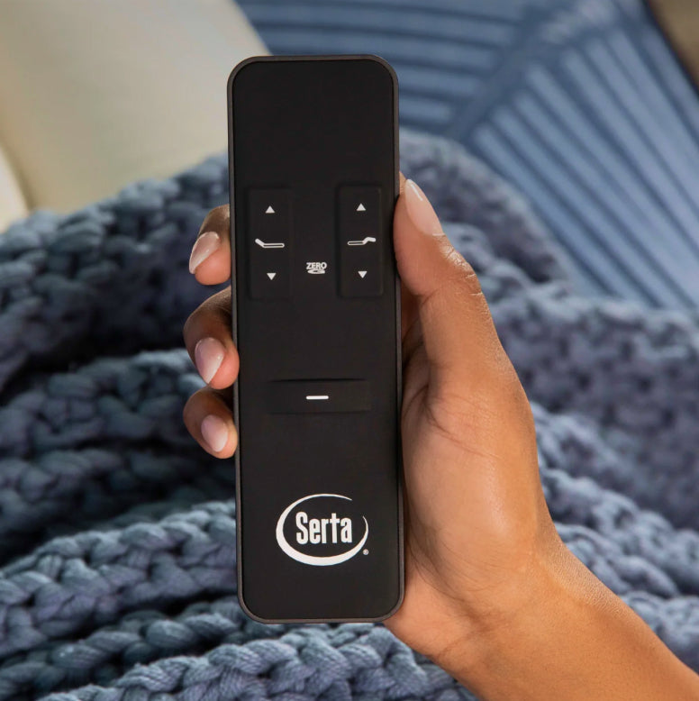 Close-up of a hand holding a Serta wireless remote, used to adjust the head and foot of an adjustable bed for customized comfort.