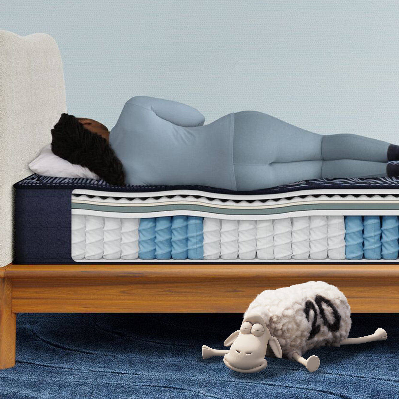 Woman sleeping on a hybrid mattress with a side cutout revealing its layered construction of coils and foam, while a Serta sheep sleeps on the floor. The mattress topper is smooth.