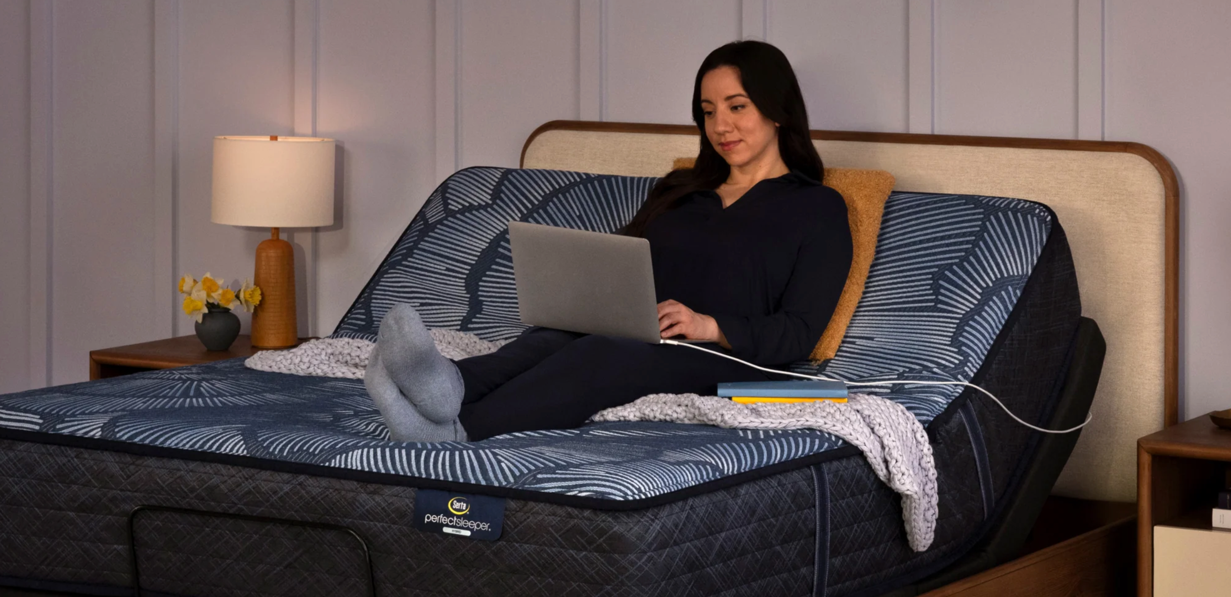 Woman working on a laptop while reclining on a Serta Perfect Sleeper adjustable bed, showcasing customizable positioning for comfort and convenience.