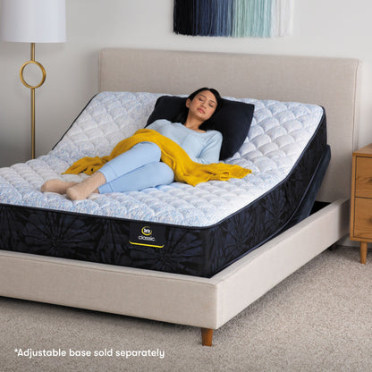 Woman laying on a Classic mattress elevated at the top as the mattress sits on an adjustable base within a beige bed frame.