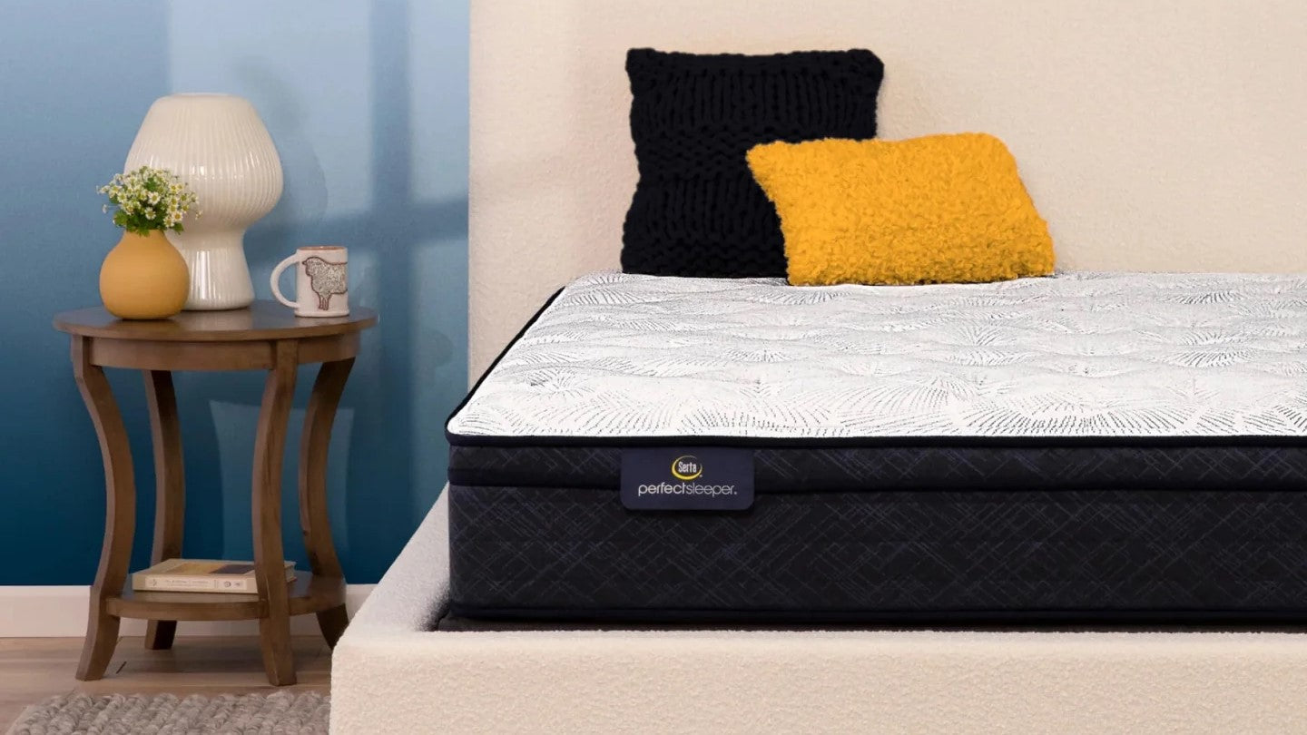 Corner of a Serta Perfect Sleeper mattress with a yellow and blue pillow on top of it